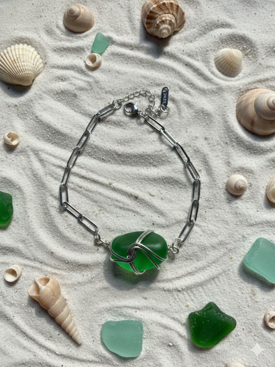 Bracelet with green sea glass piece on sand with seashells