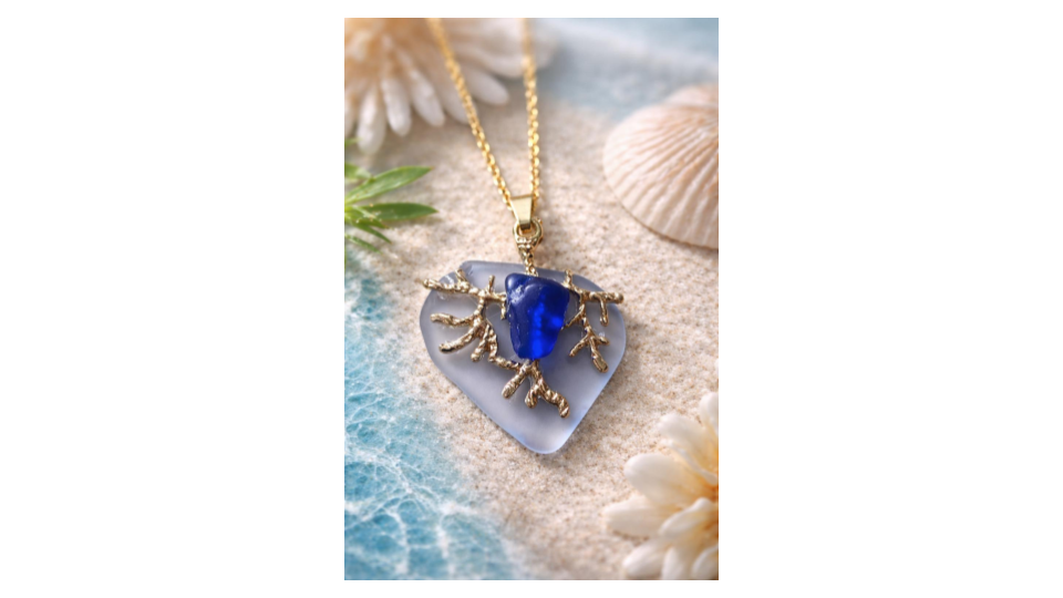 Necklace in the shape if a heart in gold over light blue sea glass with a cobalt blue sea glass pebble in the center