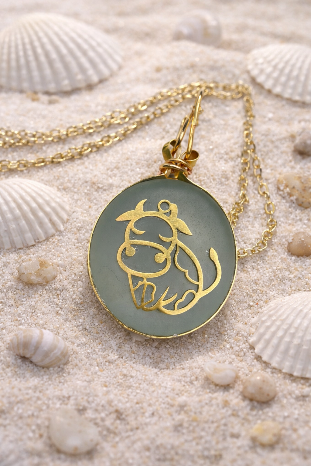 Gold necklace with a circular pendant featuring a horse design on a sandy background with shells.