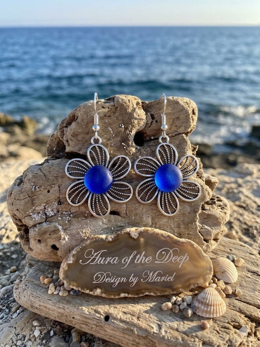 Floral earrings with blue centers on a stone with 'Aura of the Deep' inscription, ocean background
