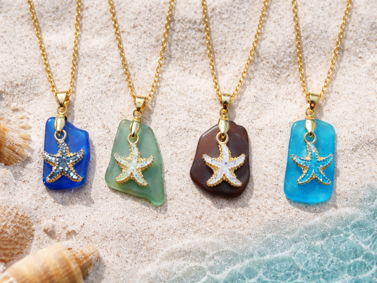 Four starfish pendants on colorful stones with gold chains on a sandy background.