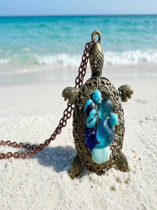 Tortoise-shaped necklace with blue and green stones on a sandy beach
