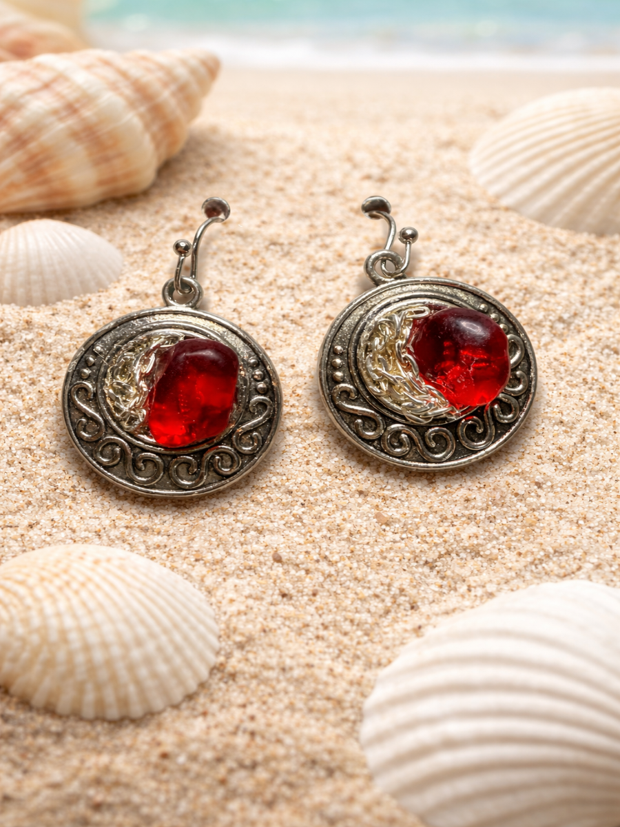 Pair of silver earrings with red stones on a sandy background with shells.