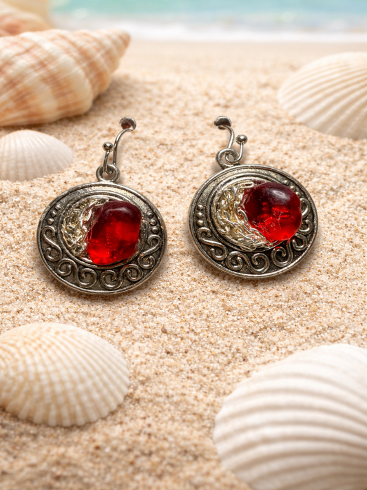Pair of silver earrings with red stones on a sandy background with shells.