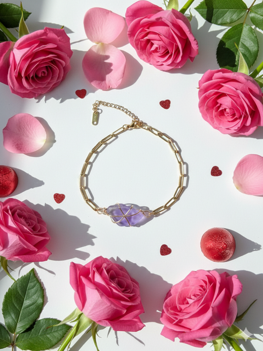Gold bracelet with a purple heart charm surrounded by pink roses and green leaves on a white background