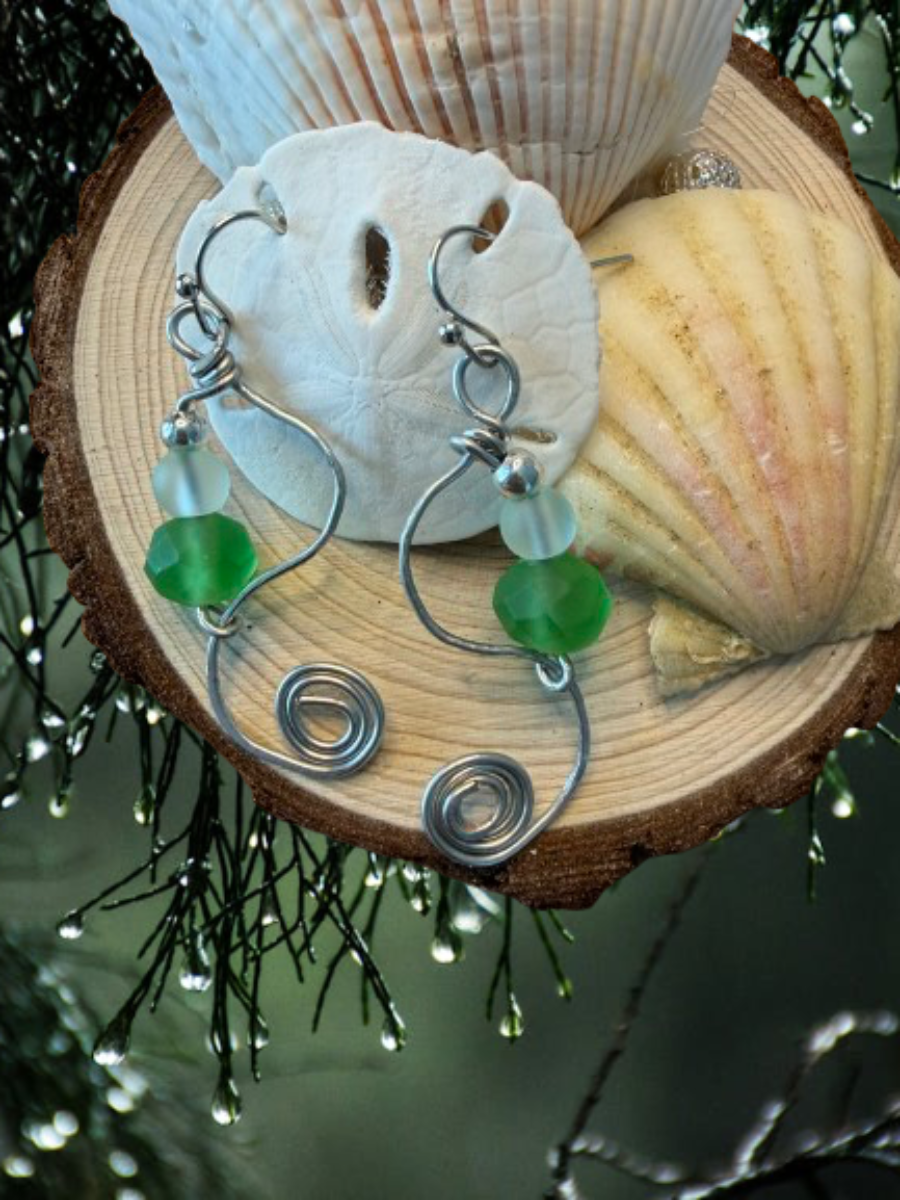 Pair of silver earrings with green beads on a wooden surface with shells.