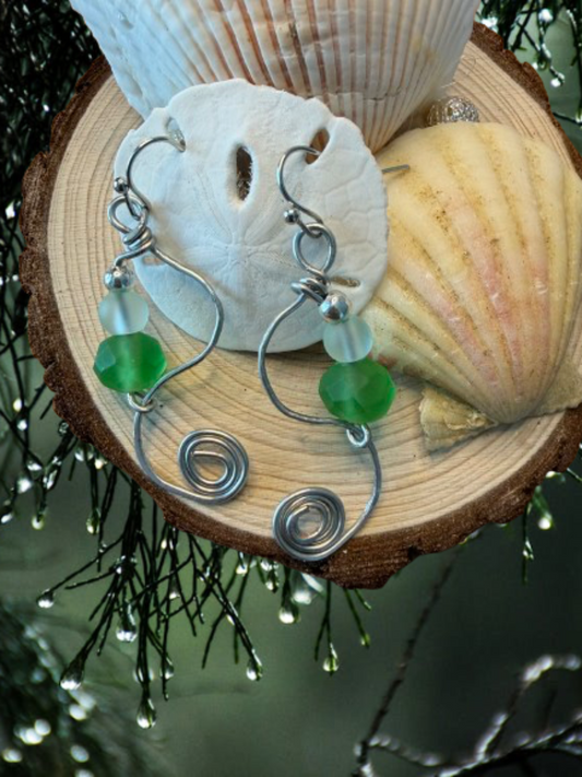 Pair of silver earrings with green beads on a wooden surface with shells.