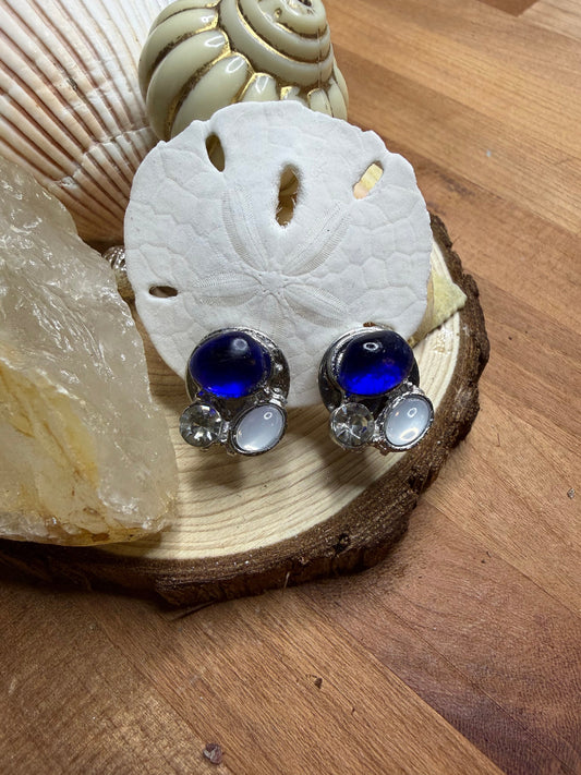 Pair of silver earrings with blue stones on a wooden surface with shells.