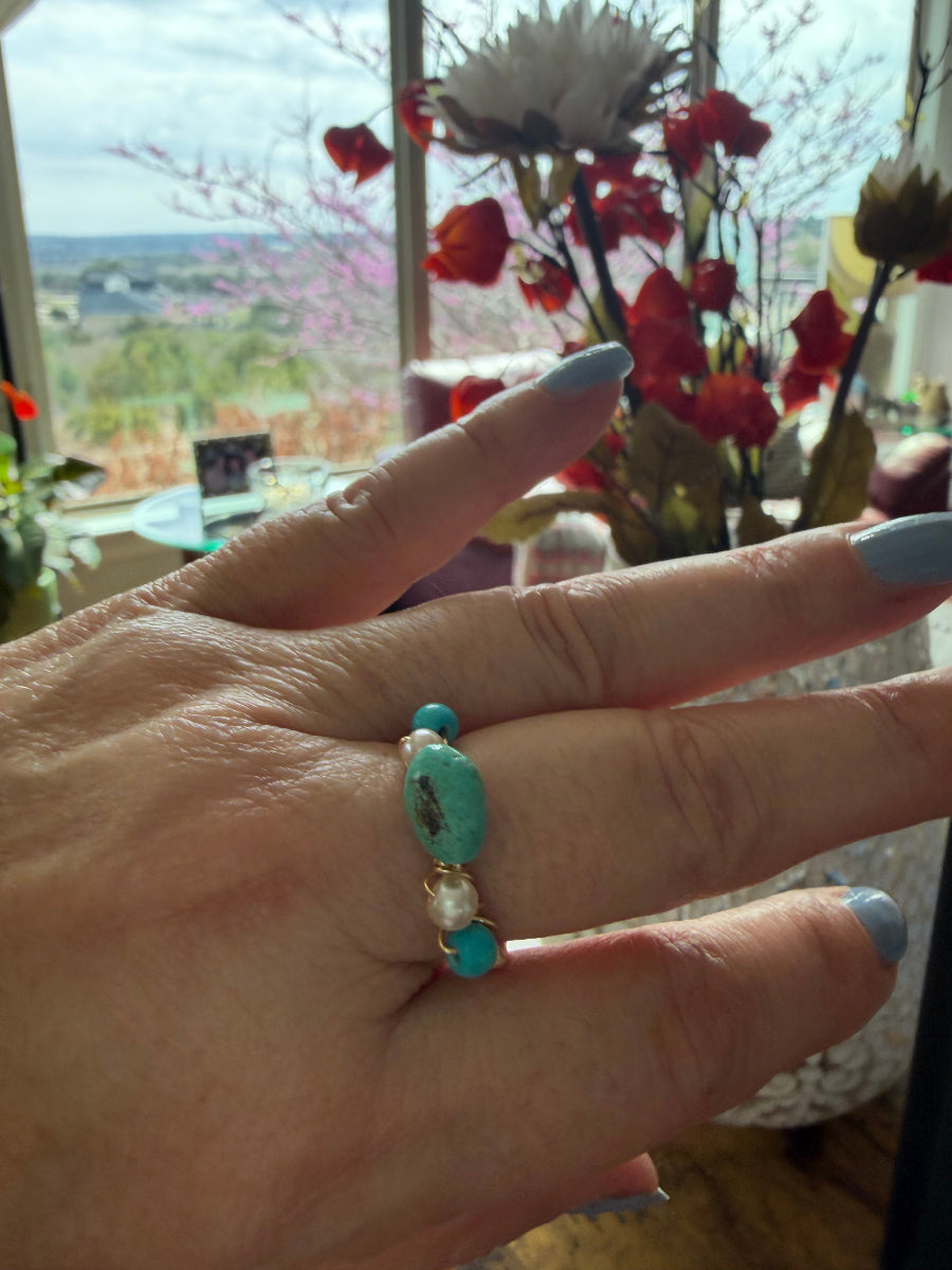 Hand wearing a turquoise beaded ring with a blurred indoor background
