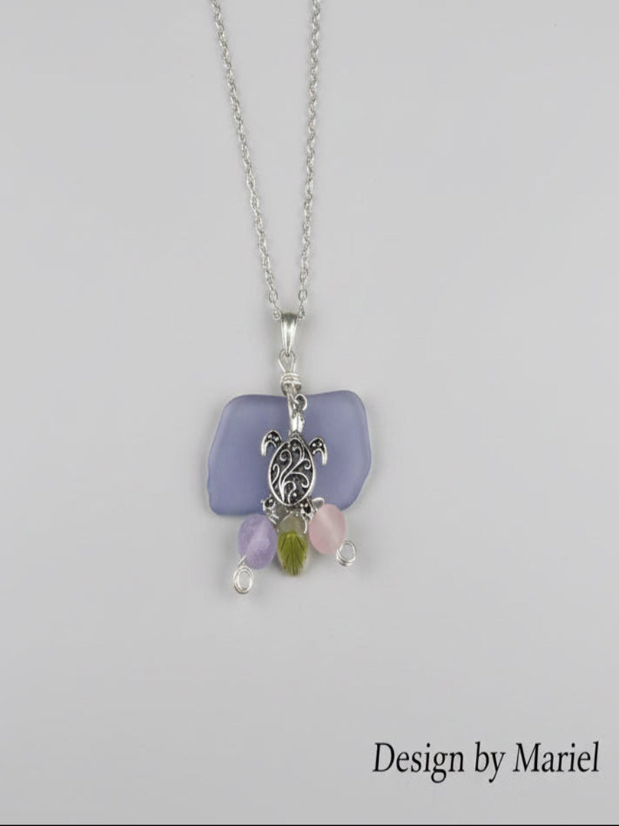 Necklace with turtle charm and sea glass pendant on a wooden surface