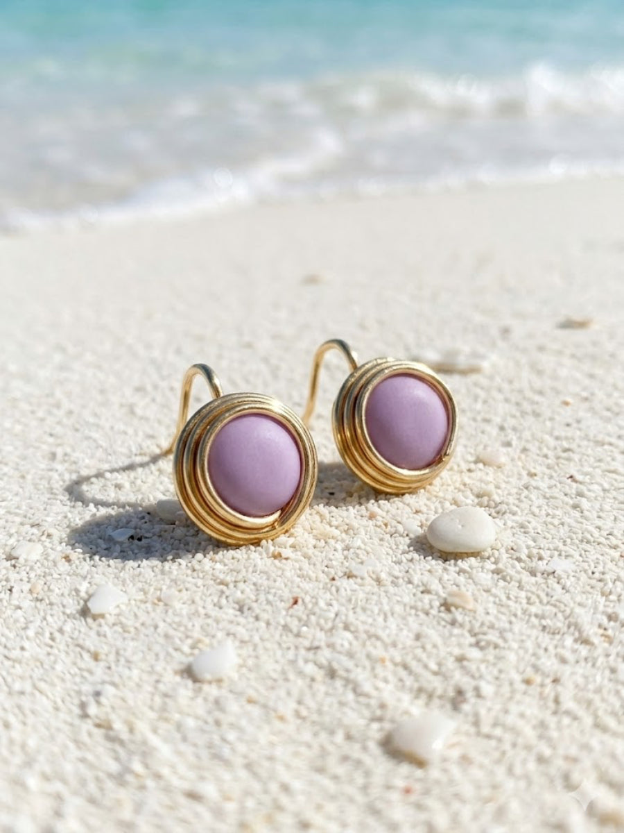 Gold earrings with purple stones on a sandy beach